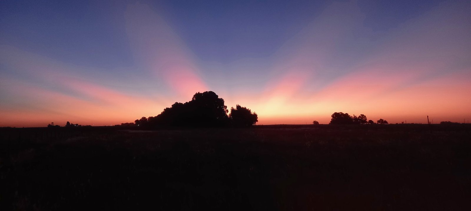 Atardecer bonaerense con rayos de sol detrás de un monte.